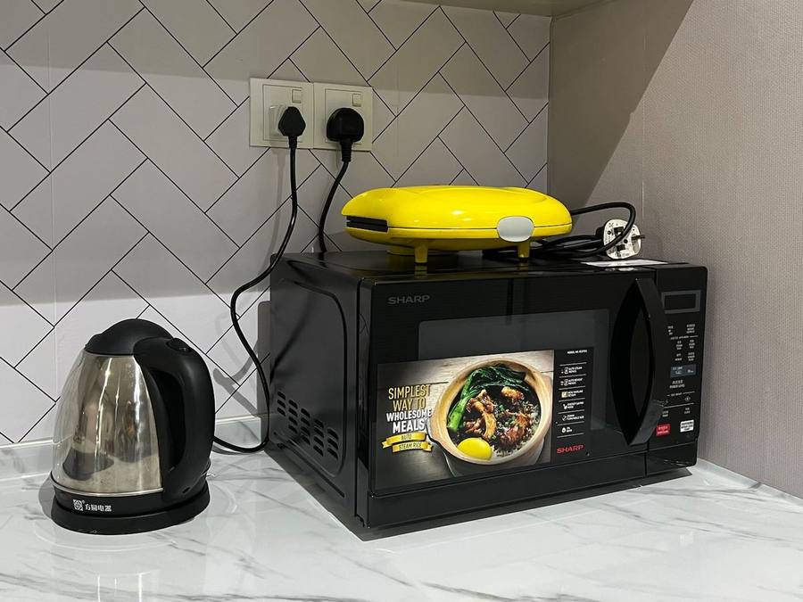 Worktop with a microwave, kettle and sandwich griller against a herringbone tiled wall.